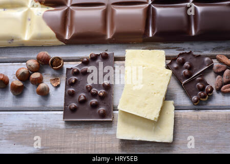 Stücke der Fliese Schokolade, Nüssen und Kakaobohnen auf hölzernen Hintergrund Stockfoto