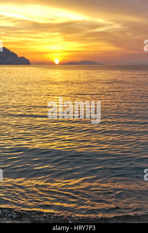 Sonnenuntergang am Strand mit schönen dramatischen gelben und orangefarbenen Himmel. Silhouette einer Insel weit im Voraus in Sicht. Stockfoto