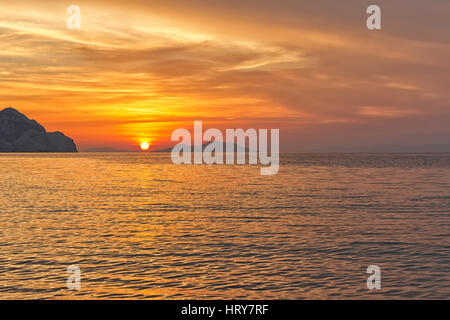 Sonnenuntergang am Strand mit schönen dramatischen gelben und orangefarbenen Himmel. Silhouette einer Insel weit im Voraus in Sicht. Stockfoto