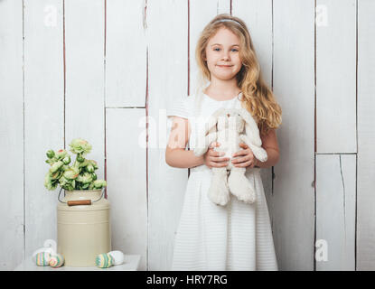 Niedliche kleine Mädchen mit Hase Kaninchen Spielzeug auf weißem Holz Hintergrund. Stockfoto