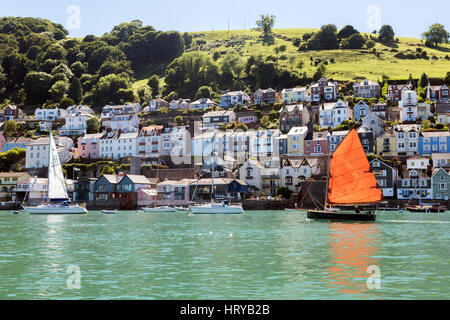 Eine Yacht mit hellen Segel macht seinen Weg nach unten der Fluss Dart vorbei an den Fluss vorderen Häusern in Dartmouth, Devon, England, UK Stockfoto