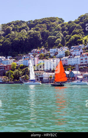 Eine Yacht mit hellen Segel macht seinen Weg nach unten der Fluss Dart vorbei an den Fluss vorderen Häusern in Dartmouth, Devon, England, UK Stockfoto