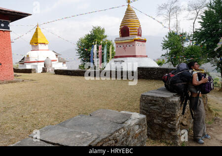 Eine müde Porter mit riesigen Taschen nimmt eine Pause neben einem Stupa auf einer Wanderung in Nepal Stockfoto