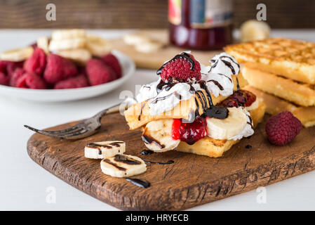 Belgische Waffeln mit Himbeeren, Bananen und Sahne auf rustikalen Tisch. Stockfoto