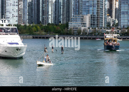 Ein Mann gekleidet wie ein Pirat in ein weißes Boot mit einem großen schwarzen Boot mit Segel nach unten und zwei Personen auf Paddel-gejagt wird. False Creek, Vancouver, BC. Stockfoto