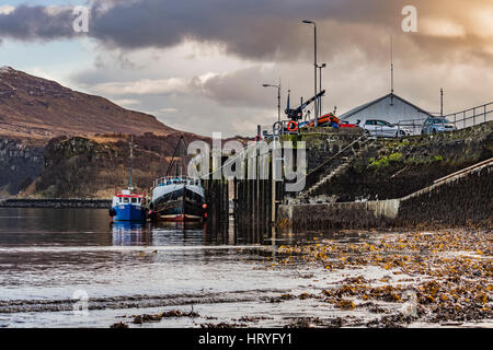 Ben Tianavaig durch den Hafen von Portree, auf der Isle Of Skye, Schottland, gegen einen dramatischen Himmel, hinter das Ende der Hafenpier und Boote Stockfoto