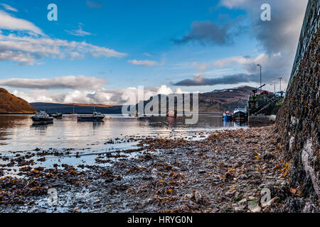 Ben Tianavaig und Sound of Raasay über Loch Portree, auf der Isle Of Skye, Schottland, gegen einen dramatischen Himmel, Blick vom Hafen auf Pier und Boote Stockfoto