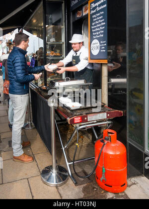 Thompsons Metzger-Shop in Northallerton High Street verkaufen heiße gekochtes Essen zu einem Mann aus einem street Grill auf einem anstrengenden Freitag Markttag Stockfoto