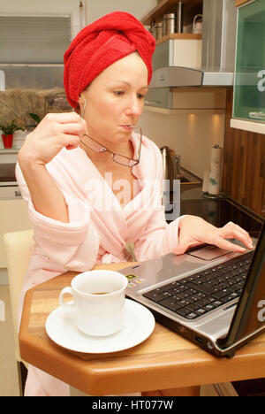 Junge Frau Im Morgenmantel Sitzt eine der Kuechenbar Und Arbeitet bin Notebook - junge Frau zu Hause mit Laptop Stockfoto