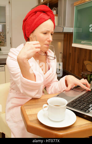 Junge Frau Im Morgenmantel Sitzt eine der Kuechenbar Und Arbeitet bin Notebook - junge Frau zu Hause mit Laptop Stockfoto