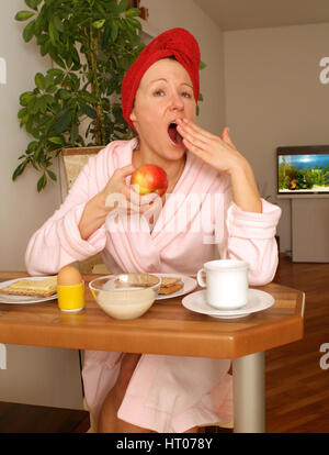 Junge Frau Im Morgenmantel Sitzt Beim Fruehstueck Und Gaehnt - junge Frau im Bademantel klaffende beim Frühstück Stockfoto