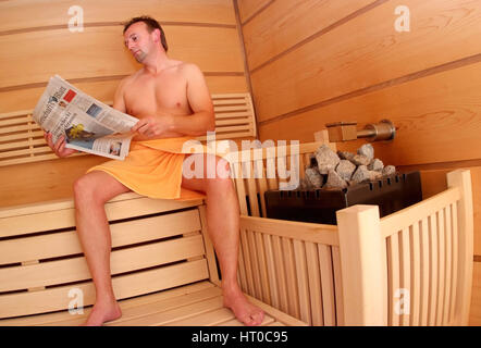 Mann liest Zeitung im Sauna - Frau in Sauna Stockfoto