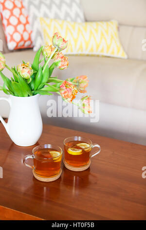 Schöne orange Tulpen Bukett mit zwei Tassen Tee auf Holztisch im Wohnzimmer Stockfoto