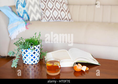 Topf mit Sukkulenten und aufgeschlagenes Buch mit dem Tee auf Holztisch. Gemütliche Zimmer Stockfoto