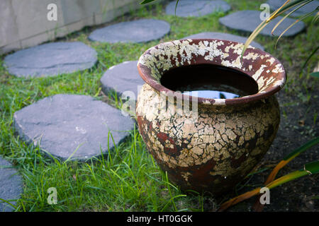 Alten strukturierten Ton Vase mit Regenwasser im Innenhof des Gartens in der Nähe der Weg von Steinen. Stockfoto