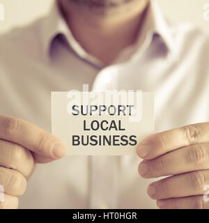 Closeup auf Geschäftsmann hielt eine Karte mit Text Unterstützung regionaler Betrieb, Business Konzept Bild mit soft-Fokus-Hintergrund und Vintage-Ton Stockfoto