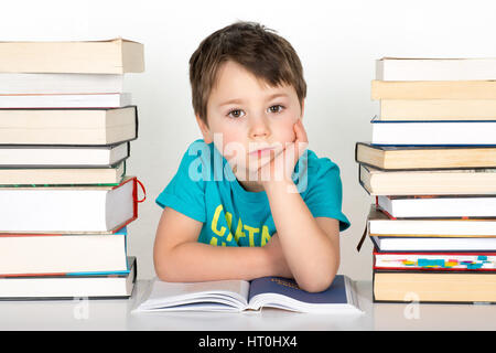 Gelangweilte Junge sitzt zwischen Stapel Bücher. Isoliert auf weißem Hintergrund. Stockfoto
