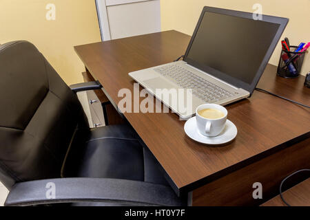 Komfortablen Arbeitsplatz im Büro mit Holztisch, schwarze Ledersessel, Laptop und Tasse Kaffee. Stockfoto