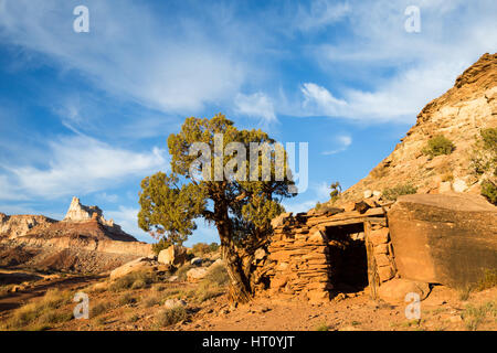 Kleines Gebäude zwischen einem Felsblock und große Wacholder unter Tempelberg im südlichen Utah. Die Bergbaulager im Bereich San Rafael Swell produziert Stockfoto