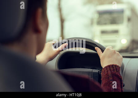Frau fährt Auto in Richtung eines großen LKW auf der Straße, selektiven Fokus auf Händen greifen das Lenkrad des Fahrzeugs, Retro-getönten Bild Stockfoto