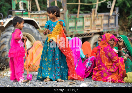 Zwei Kinder stehen unter den sitzen Frauen in lebendigen traditionellen Rajasthani Kleidung Stockfoto