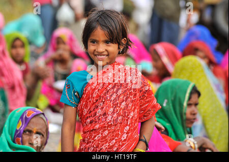 Eine junge Rajasthani Mädchen in einer lebendigen bestickt traditionelles Kleid steht unter einer Gruppe von sitzenden Frauen Stockfoto