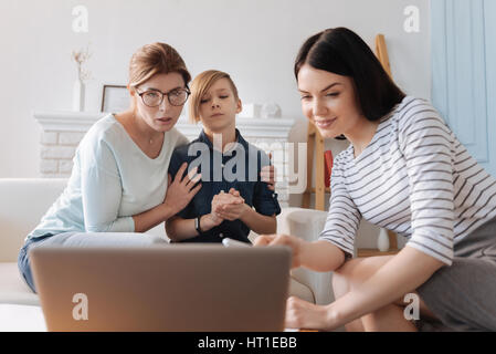 Zeigen Sie es erneut. Sehr überrascht Mutter tragen legere Kleidung, umarmt ihr Sohn während der Suche auf dem Bildschirm des Computers Stockfoto