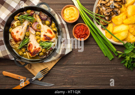 Abendessen mit gebackene Hähnchenschenkel mit Oliven gewürzt mit aromatischen Kräutern und Kartoffeln mit Pilzen auf einem rustikalen Hintergrund. Ansicht von oben, Raum zu kopieren. Stockfoto