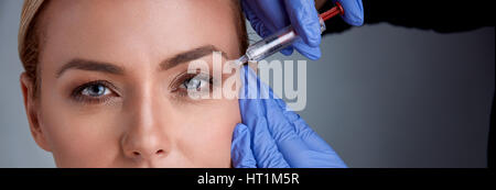 Frau fröhlich mittleren Alters ist immer Botox Verfahren, Arzt in ihrer Nähe steht und Spritze halten und berühren, weibliches Gesicht Stockfoto