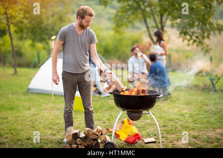 Junger Mann legen Stamm Grill Feuer auf Campingplatz Stockfoto