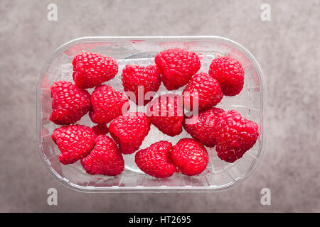 frische reife Himbeeren in Plastikbehälter auf grau Stockfoto