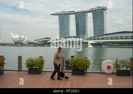 08.10.2016, Singapur, Republik Singapur - eine Putzfrau fegt den Outdoor-Bodenbelag eines Restaurants mit der Marina Bay Sands Hotel hinter. Stockfoto