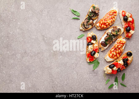 Große Auswahl an kleinen Bruschetta mit Caprese Salat, weißen Bohnen auf dem Grill mit Tomatensauce und gebratene Pilze mit Frischkäse, serviert auf graue Rückseite Stockfoto