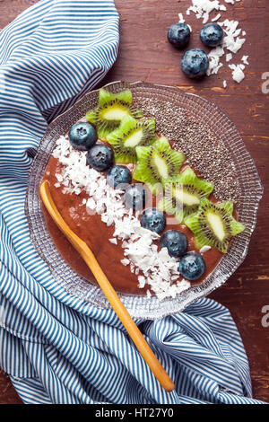 Schoko-Bananen-Smoothie Schüssel garniert mit Heidelbeeren, Kiwi, Chia-Samen, Kokos Flocken für gesundes Frühstück. Superfood Stockfoto