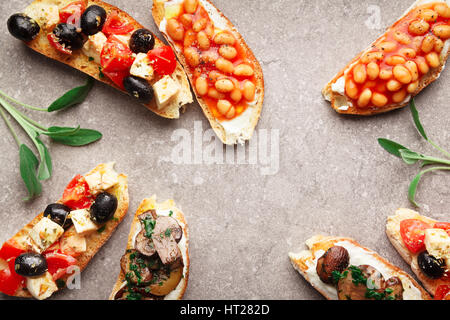 Große Auswahl an kleinen Bruschetta mit Caprese Salat, weißen Bohnen auf dem Grill mit Tomatensauce und gebratene Pilze mit Frischkäse, serviert auf graue Rückseite Stockfoto