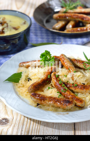 Gebratene bayerische Würstchen aus Nürnberg serviert auf Sauerkraut, Kartoffelpüree und einige andere Würste im Hintergrund Stockfoto