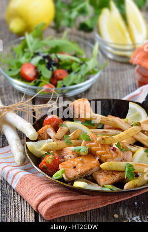 Gebratenem weißen Spargel mit gebratenem Lachs, serviert in einer eisernen Pfanne mit einem Rucola-Salat Stockfoto