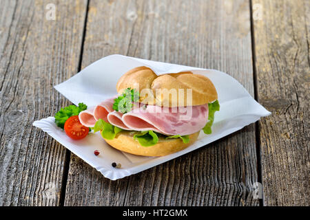 Knusprige Brötchen mit in Scheiben geschnittenen Schinkenwurst auf einen Pappteller mit einer Serviette Stockfoto