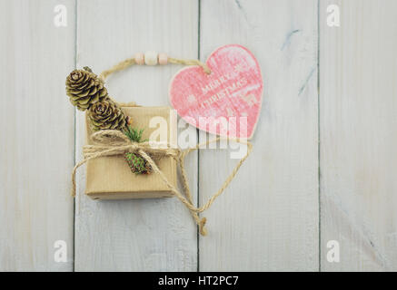 Zwei Boxen mit einem Geschenk auf einem Holztisch gebunden mit Bindfäden und dekoriert mit einem Zweig von Christmas tree mit Tannenzapfen und Herz aus Holz mit einer Schrift Stockfoto