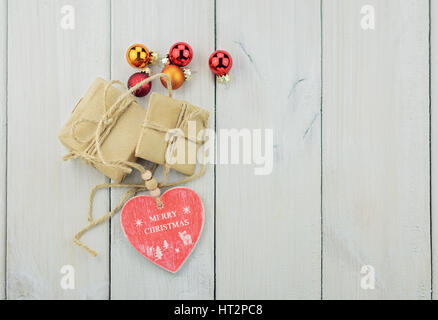 Zwei Boxen mit einem Geschenk auf einem Holztisch mit einem Seil gefesselt und mit Weihnachtskugeln, Herz aus Holz mit einer Inschrift verziert. Stockfoto