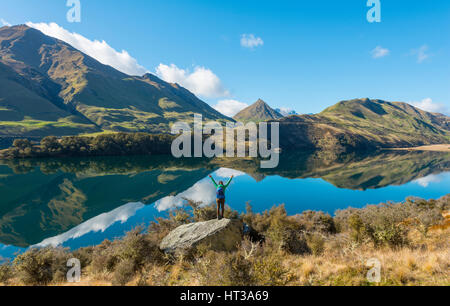 Wanderer stehen auf Felsen streckte die Arme, Berge im Lake Moke Lake in der Nähe von Queenstown, Otago Region und Southland Stockfoto