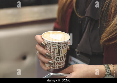 Geschäftsfrau hält in ihrer Hand Tasse Cappuccino mit Herz bei einem Business-Meeting (reduzierte Ton) Stockfoto