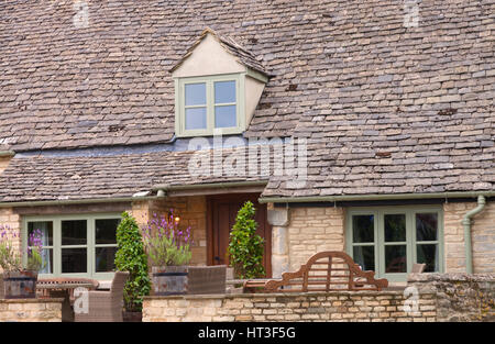 Englisches Landhaus aus Stein mit Lavendel in Fässern, Gartenbank, Stühle in der Front in einem ländlichen Dorf Cotswolds, an einem sonnigen Sommertag. Stockfoto