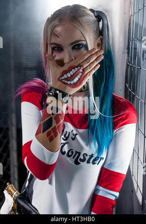 Porträt der lächelnde Mädchen in Tracht Harley Quinn. Sie ist in der Nähe von Raster. Sie schließt den Mund mit der Hand. Hautnah. Cosplay. Stockfoto