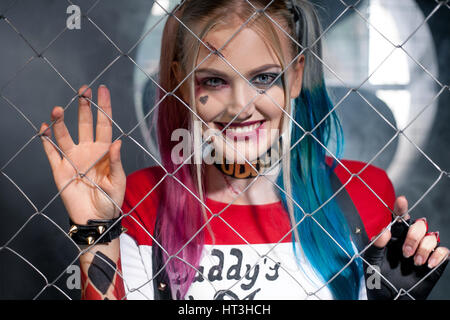 Porträt der lächelnde Mädchen in Tracht Harley Quinn. Sie schaut durch das Gitter. Hautnah. Cosplay. Stockfoto