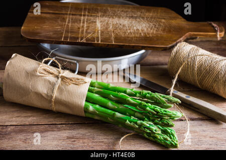Bündel von frischen Bio Spargel eingewickelt in Kraftpapier am Küchentisch, schneiden, Brett Schale Messer, Tageslicht, gemütliche Atmosphäre Stockfoto