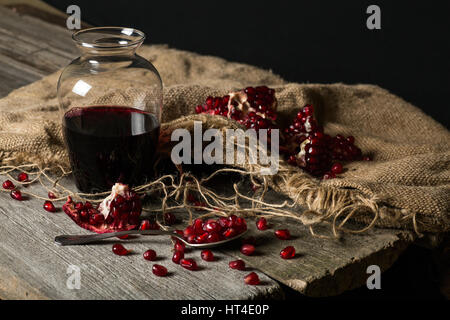 Karaffe mit Granatapfelsaft, Kerne mit einem Löffel auf einem Holztisch. Stockfoto