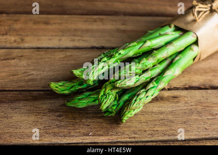 Bündel von organischen Grünspargel mit Bindfäden in Kraftpapier liegend im Alter von Plank Holztisch, Menüvorlage, Draufsicht, Textfreiraum für Text gebunden Stockfoto