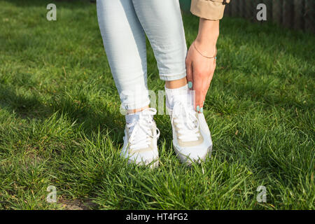 Schlanke Frauen Beine in Jeans und weiße Turnschuhe auf einem grünen Rasen an einem sonnigen Tag Stockfoto