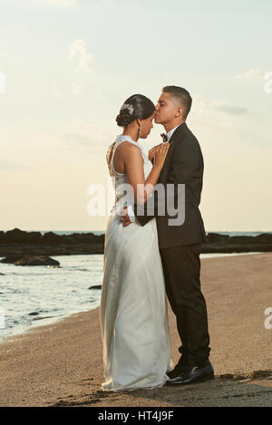 Hispanische junge Ehepaar am Hochzeitstag. Umarmt von Braut und Bräutigam am Meer Strand Sonnenuntergang Stockfoto